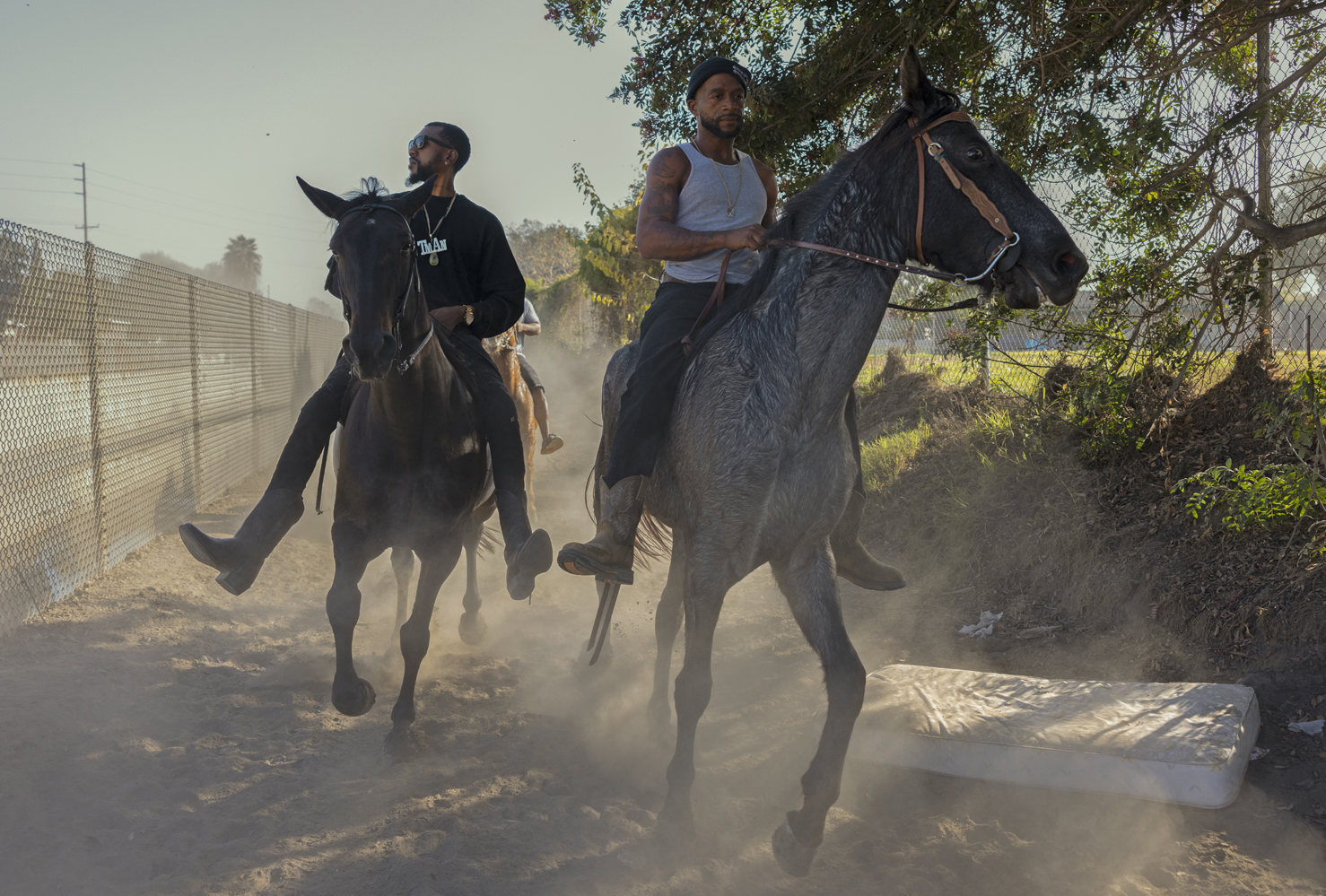 Compton Cowboys two men riding horses next to a fence in Compton