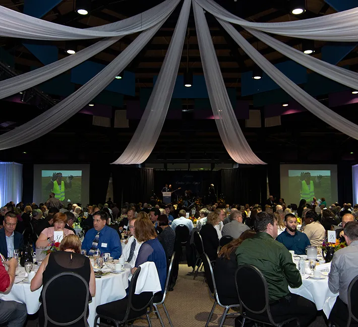 Event hall filled with Andis employees eating at tables and watching the stage