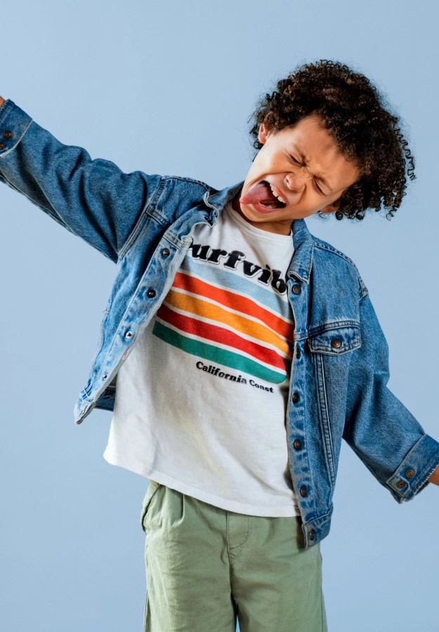 Large image of boy with curly brown hair making face wearing jean jacket