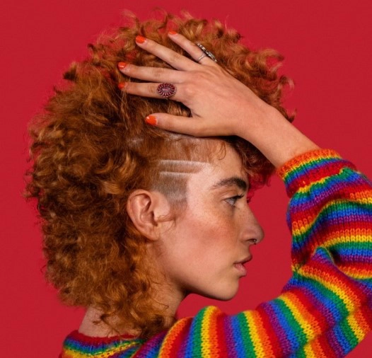 Girl with red hair, rainbow sweater running her hands through up her hair